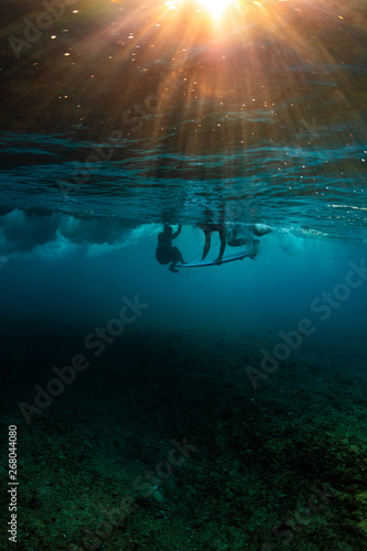 Underwater view of the surfers in the water at sunset