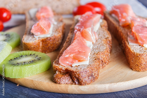 Smoked salmon sandwiches with butter on dark wooden background.