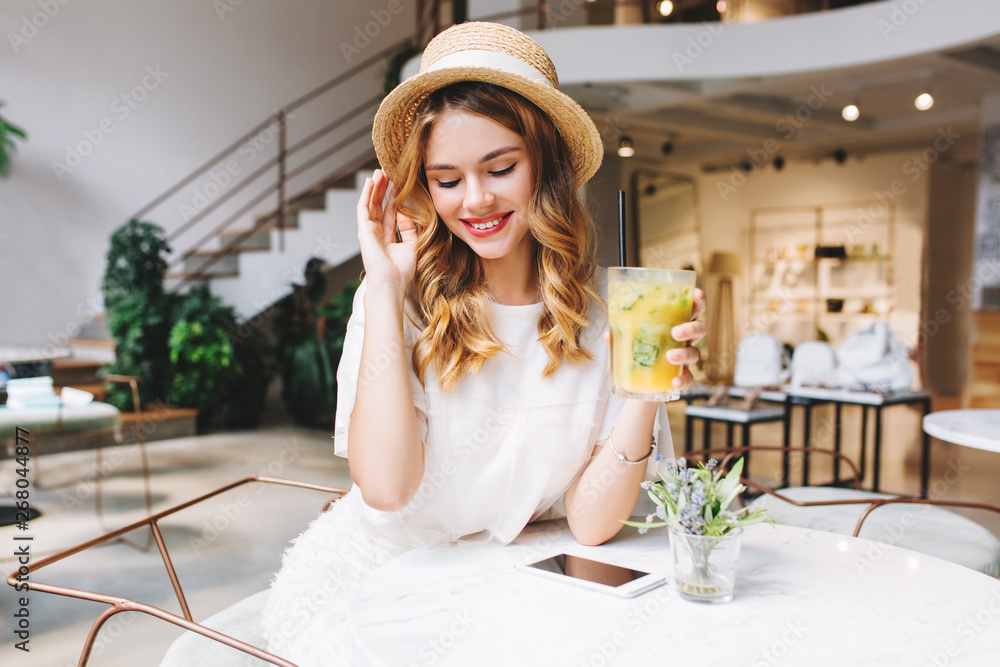 © Look! - Romantic girl with blonde curls resting in cafe and shy smiling, looking down. Indoor portrait of cute young lady in vintage hat holding glass of fruit beverage and sit at the table with phone on it. © Look! - Romantic girl with blonde curls resting in cafe and shy smiling, looking down. Indoor portrait of cute young lady in vintage hat holding glass of fruit beverage and sit at the table with phone on it.
