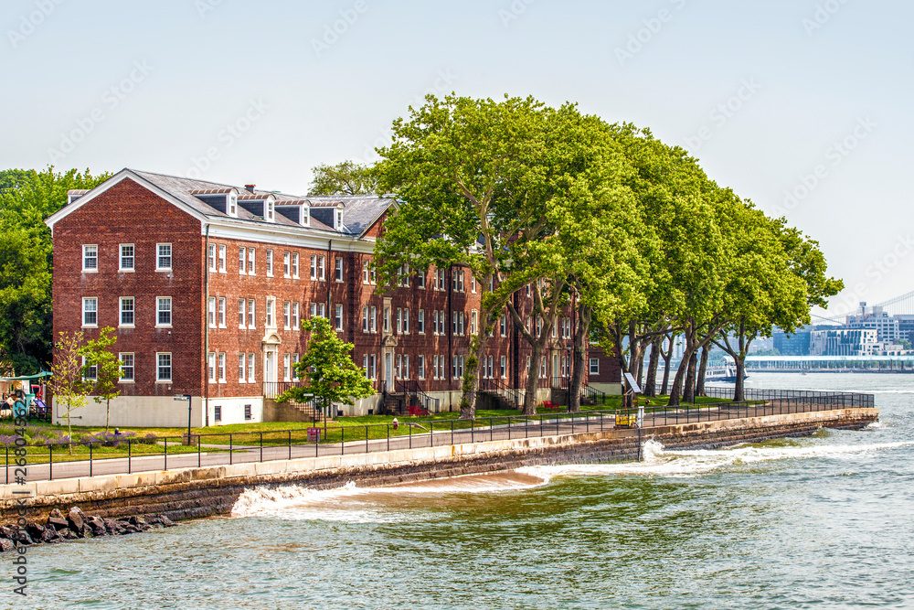 Obraz premium Governors Island and red old retro brick buildings near fort Jay separated from Brooklyn by Buttermilk Channel during sunny summer day in New York City, USA