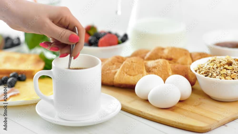 Close-up European female hand mixing morning coffee beverage in white cup using spoon side view Close-up European female hand mixing morning coffee beverage in white cup using spoon side view