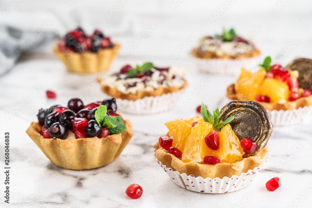 Fruit tart with orange, pomegranate, currant and cream, cakes and sweetness on light marble background. Delicious dessert and candy bar Fruit tart with orange, pomegranate, currant and cream, cakes and sweetness on light marble background. Delicious dessert and candy bar