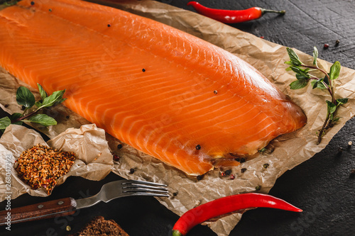 Obraz na płótnie Smoked fillet salmon, red fish steak with spices and lemon on craft paper over dark stone background