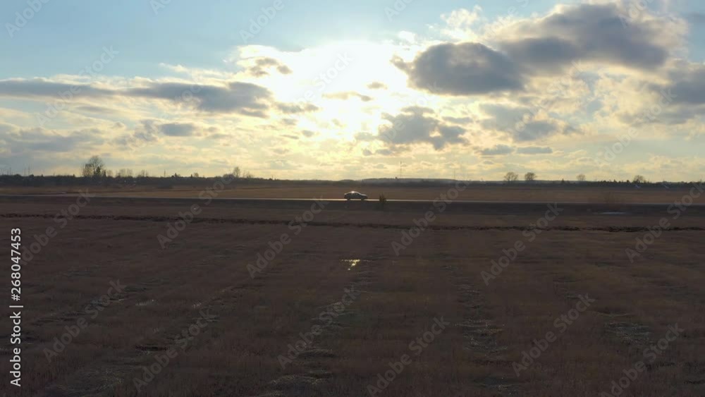 Aerial view car rides on the road in the field at sunset. The drone follows the car in profile. Aerial view car rides on the road in the field at sunset. The drone follows the car in profile.