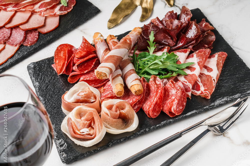 Antipasto platter cold meat with grissini bread sticks, prosciutto, slices ham, beef jerky, salami on slate stone board over marble background. Meat appetizer. Antipasto platter cold meat with grissini bread sticks, prosciutto, slices ham, beef jerky, salami on slate stone board over marble background. Meat appetizer.