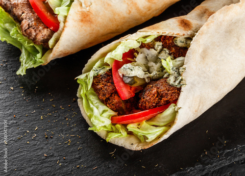 Canvas Print Tortilla wraps with roasted chickpeas falafel patties, fresh vegetables and salad on black stone background