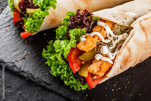 Photography Tortilla wraps with grilled chicken fillet, fresh vegetables and salad on black stone background