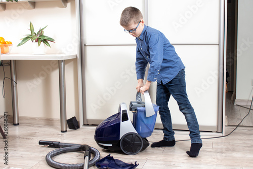Chłopiec przygotowuje odkurzacz do sprzątania mieszkania.  Sprzątanie mieszkania. Chłopiec wkłada pojemnik z wodą do odkurzacza.