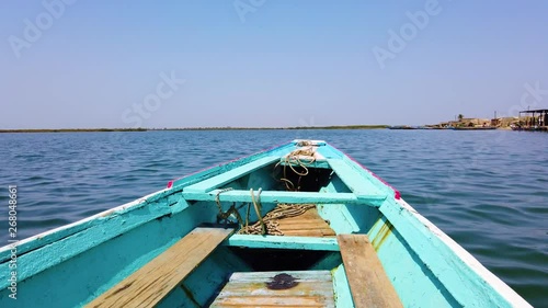 4K video of Wooden blue and white canoe floats on water surface. It is a sea lagoon in Africa, Senegal. It is birds national park.  photo