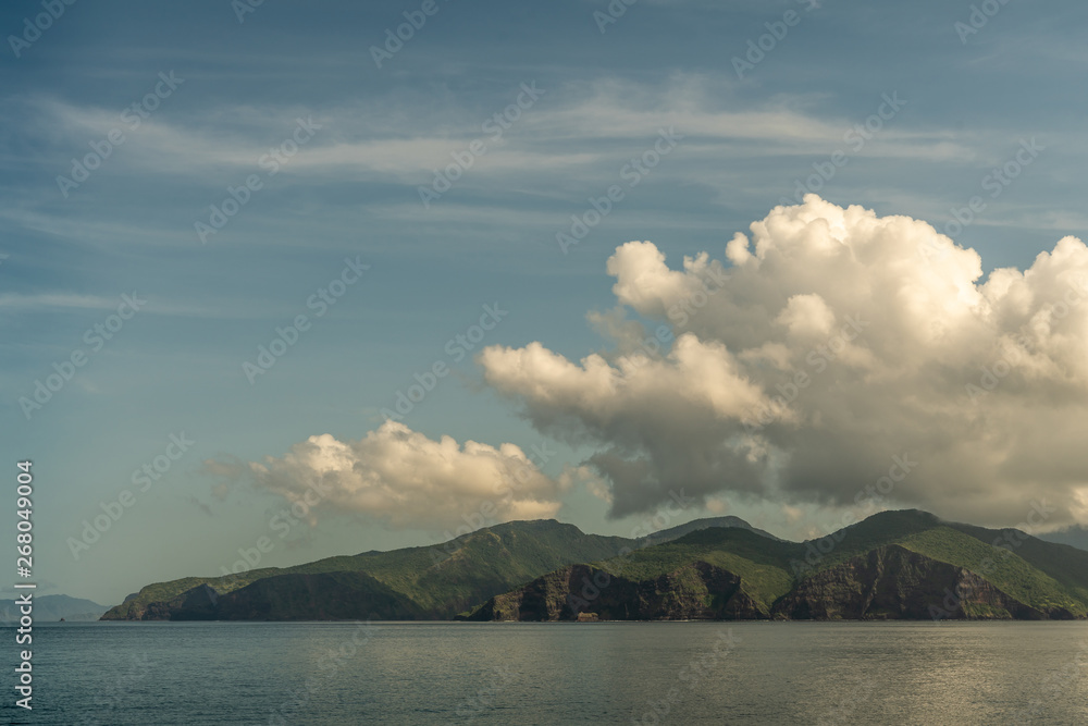 Rinca Island, Indonesia - February 24, 2019: Early morning. Southside coast in Savu Sea under cloudscape with white and darker patches.Green hills and cliffs.