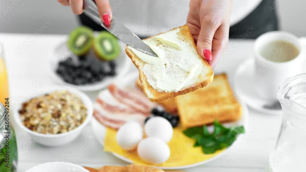 Woman hand spreading creamy butter on fresh appetizing toast using knife close-up Woman hand spreading creamy butter on fresh appetizing toast using knife close-up