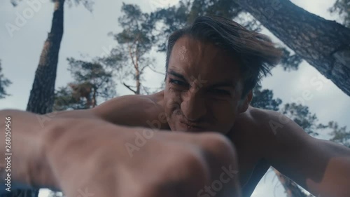 Crazy aggressive shirtless man beats with his fists the lying person outdoor at forest