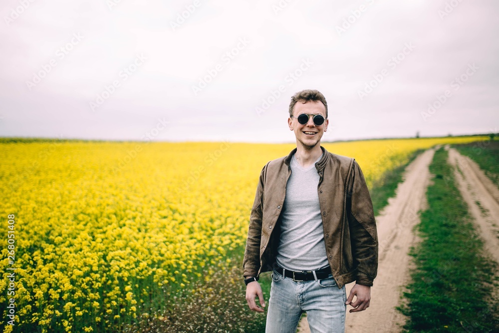 man wearing round steampunk sunglasses and a brown leather jacket in a summer yellow flowered field man wearing round steampunk sunglasses and a brown leather jacket in a summer yellow flowered field