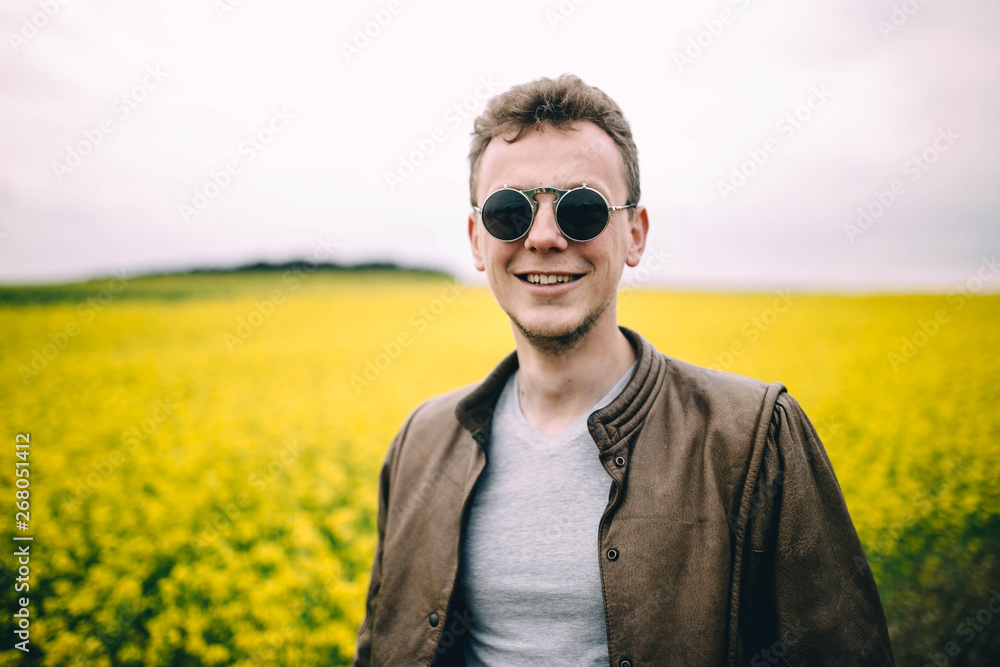 man wearing round steampunk sunglasses and a brown leather jacket in a summer yellow flowered field man wearing round steampunk sunglasses and a brown leather jacket in a summer yellow flowered field