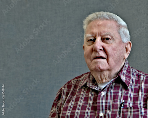 Senior octogenarian old man in plaid shirt with gray background.