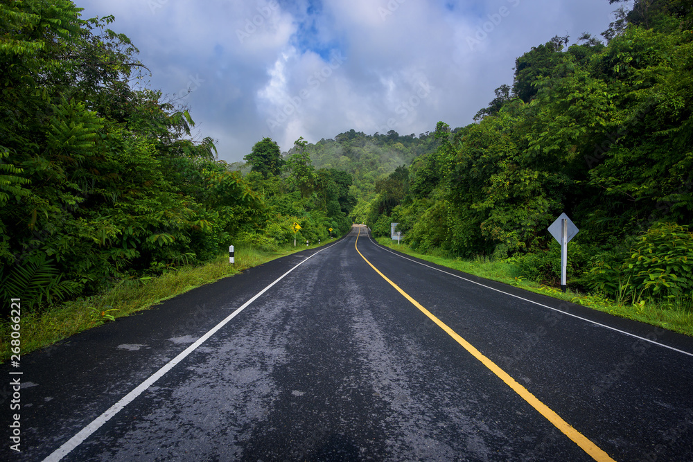 Asphalt road and mountains landscape under fog from rain with clouds