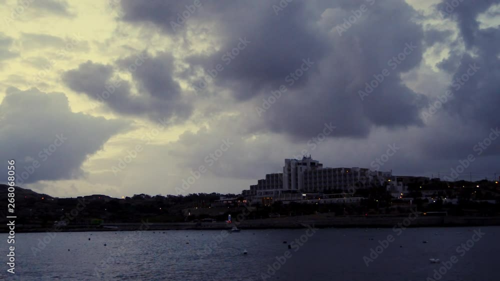 early morning in Qawra, Malta, before sunrise, rainy stormy clouds over buildings and early morning traffic early morning in Qawra, Malta, before sunrise, rainy stormy clouds over buildings and early morning traffic