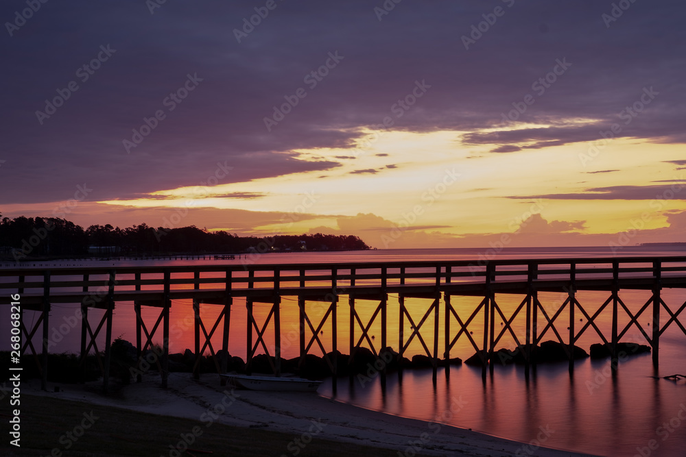 View from the shore of a long jetty in front of a beautiful sunrise at the Neuse River estuary at a park in Minnesott Beach, North Carolina.