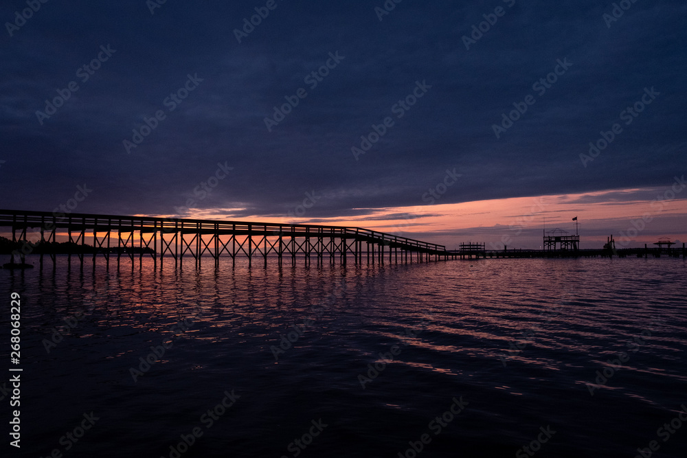 View of a long pier in front of a beautiful sunrise at the Neuse River estuary at a park in Minnesott Beach, North Carolina.