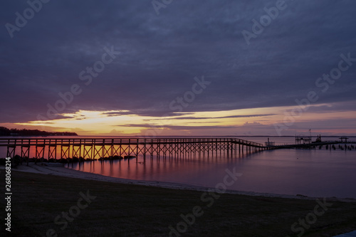 View from the shore of a long pier in front of a beautiful sunrise at the Neuse River estuary at a park in Minnesott Beach  North Carolina.