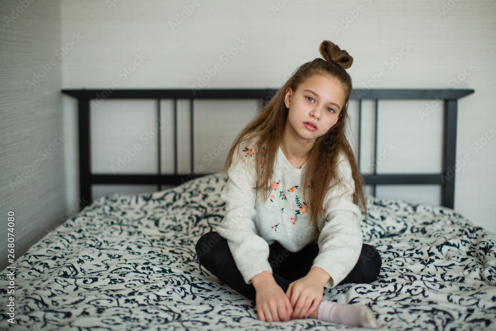Twelve year old cute girl having fun in her room sitting on the bed