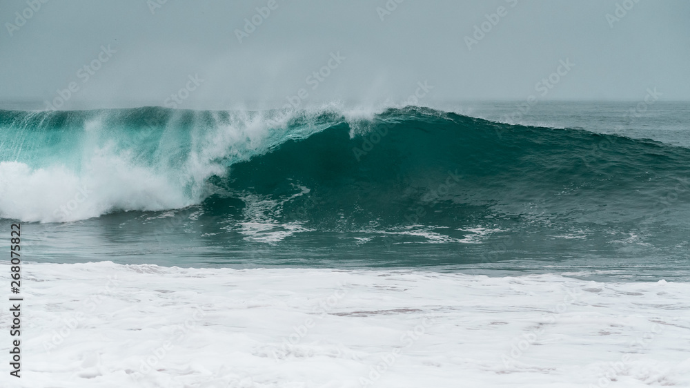 Fototapeta premium A large barreling wave crashing onto the shore spraying mist