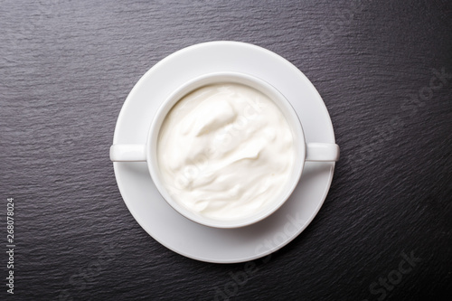 Greek yoghurt in white bowl on black slate background with copy space