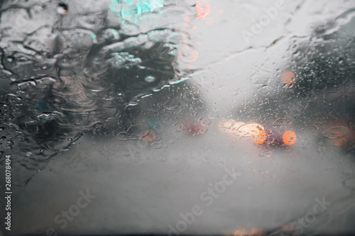 Drops Of Rain Drizzle on the glass windshield in the evening. street in the heavy rain. Bokeh Tail light and Traffic lights in city. Please drive  car carefully, slippery road. soft focus.