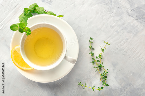 A cup of green tea with lemon, shot from above with mint, thyme, and copy space