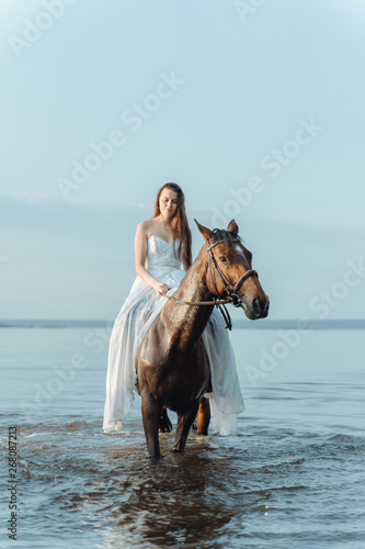 Beautiful girl in a white long dress riding a horse. Bride in the lake on horseback. © cinematri
