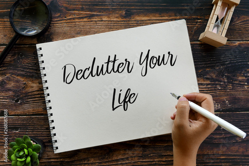 Top view of magnifying glass,sand clock,plant,pen with hand writing ' Declutter Your Life ' on notebook on wooden background.