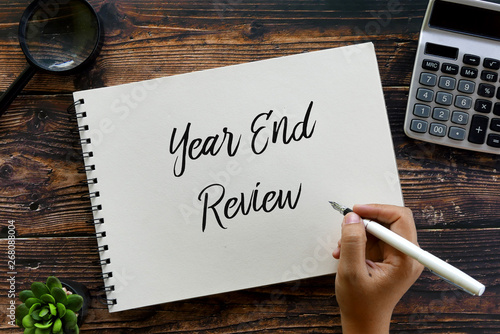 Top view of magnifying glass,calculator,plant,pen and hand writing ' Year End Review ' on a notebook on wooden background.