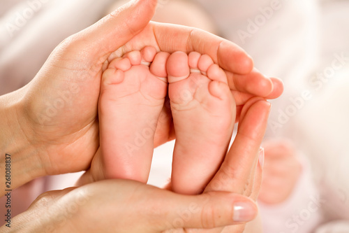 the mother holds the feet of her little baby in her palms