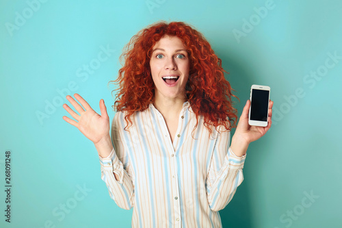 Beautiful redhead woman with mobile phone on color background