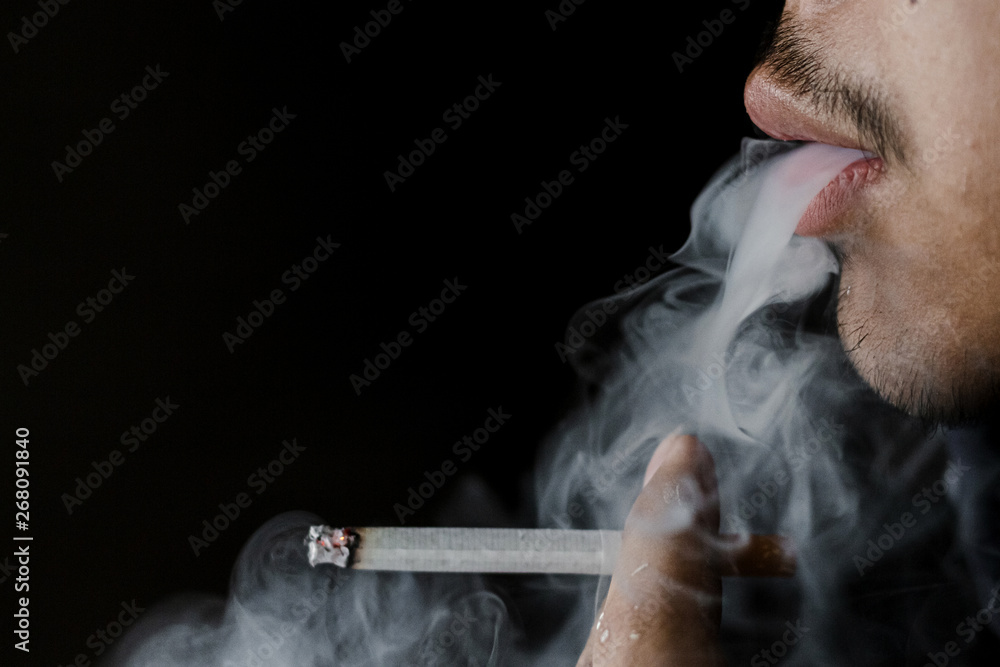 Close up portrait of young man smoking cigarette a black background