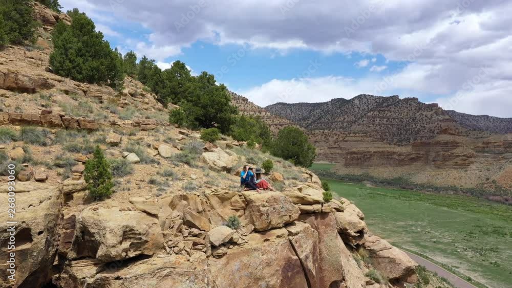 Two women sitting on edge of cliff looking over the valley while rotating around them in the Utah desert. Two women sitting on edge of cliff looking over the valley while rotating around them in the Utah desert.