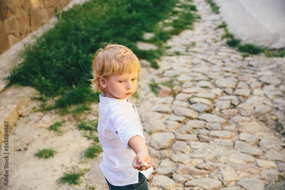 a little boy in the white clothes on the stone and grass background.
