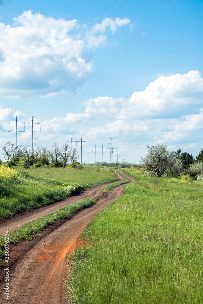 rural road between field and small forest, blue sky with clouds rural road between field and small forest, blue sky with clouds