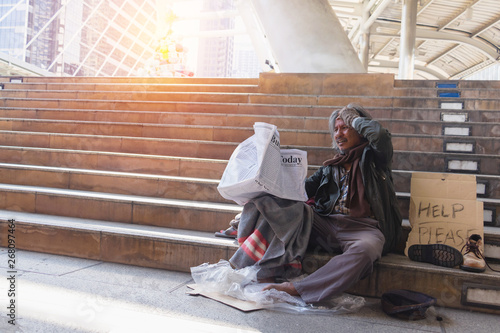 Homeless man is sitting down on staircase in town.He is read newspaper.He is very unhappy. poverty,despair, Photo Sympathetic and hope concept.