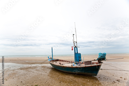 Isolated solo alone local fishing boat on tranquil peaceful beach with natural blue sky with puffy white clouds in bright clear sunny day