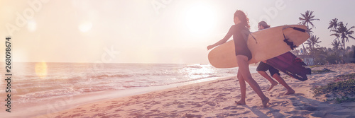 Photography Young couple of happy smiling surfers run with surfboards on ocean coast, s pano