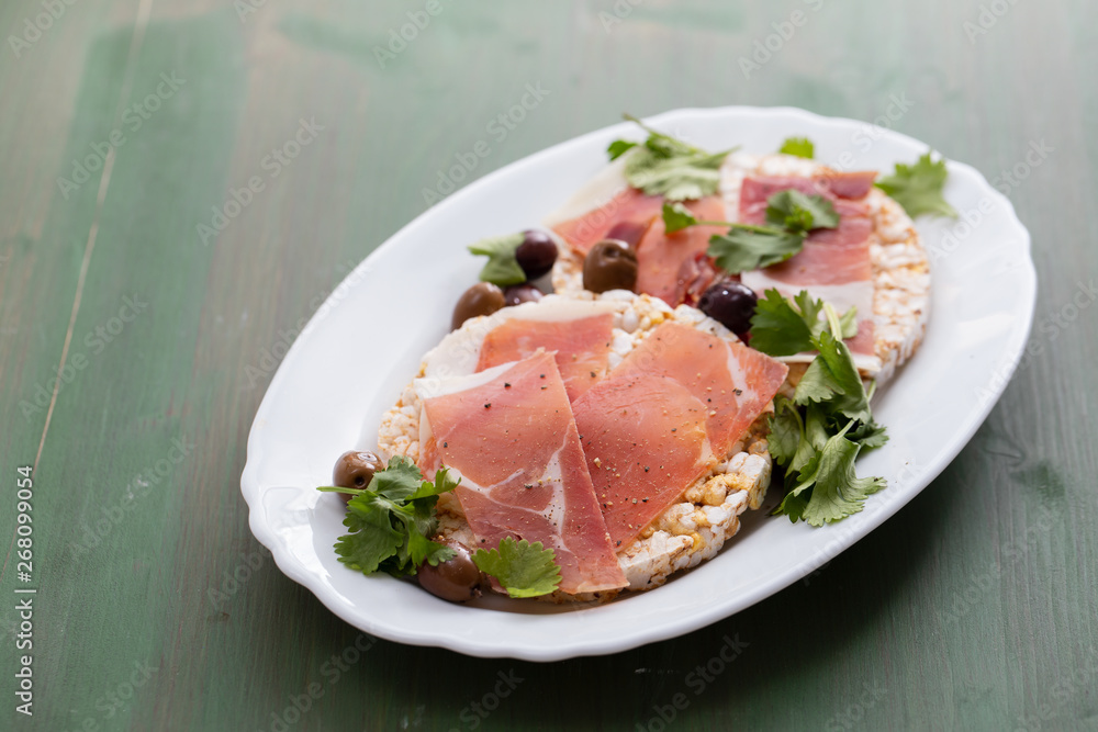 crispy rice diet toasts with prosciutto on ceramic background