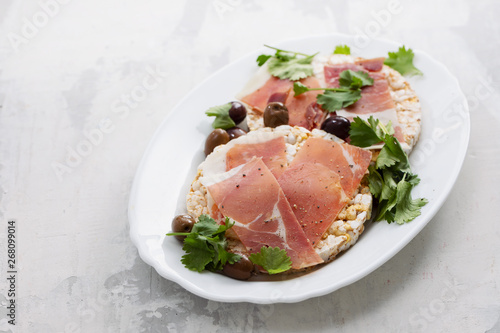 crispy rice diet toasts with prosciutto on ceramic background