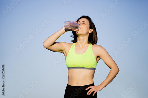 Girl drinking water wearing sporty clothes in the field