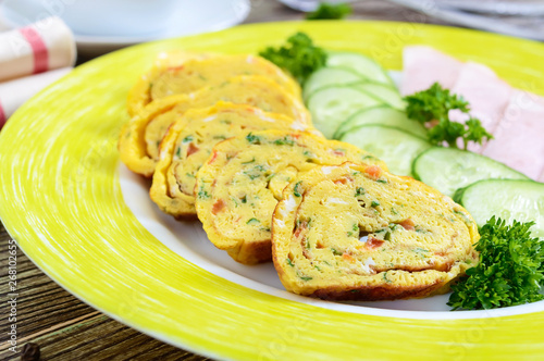 Omelette, egg roll with ham and fresh cucumber on a wooden table. Tasty healthy breakfast.