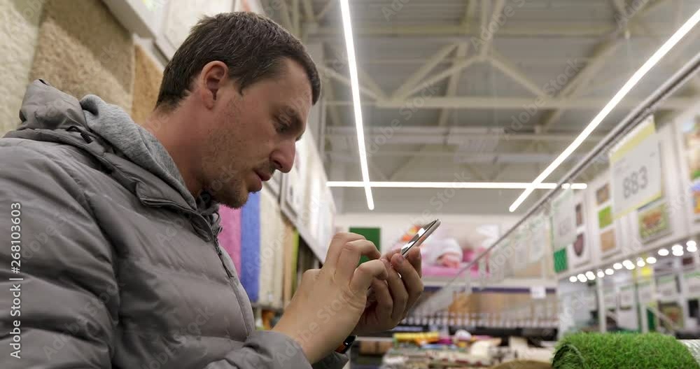 Side view of young male buyer photographing products of floor covering section indoors Side view of young male buyer photographing products of floor covering section indoors