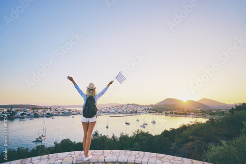 Enjoying vacation in Greece. Young traveling woman with national greek flag enjoying sunset on sea view point.
