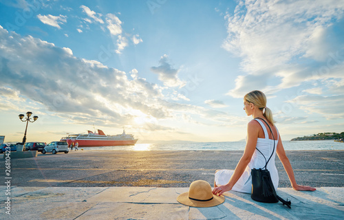 Traveling by Greece. Young happy woman enjoying beautiful sunset on the sea wharf waiting for ferry.