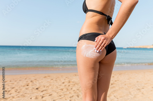 Woman hand is applying suntan cream on her buttocks at the beach at the sea background