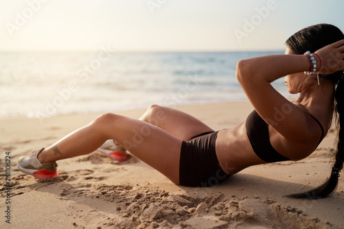 Fotografie Abs workout - fitness woman working out on beach doing abs exercises for stomach weight loss toning